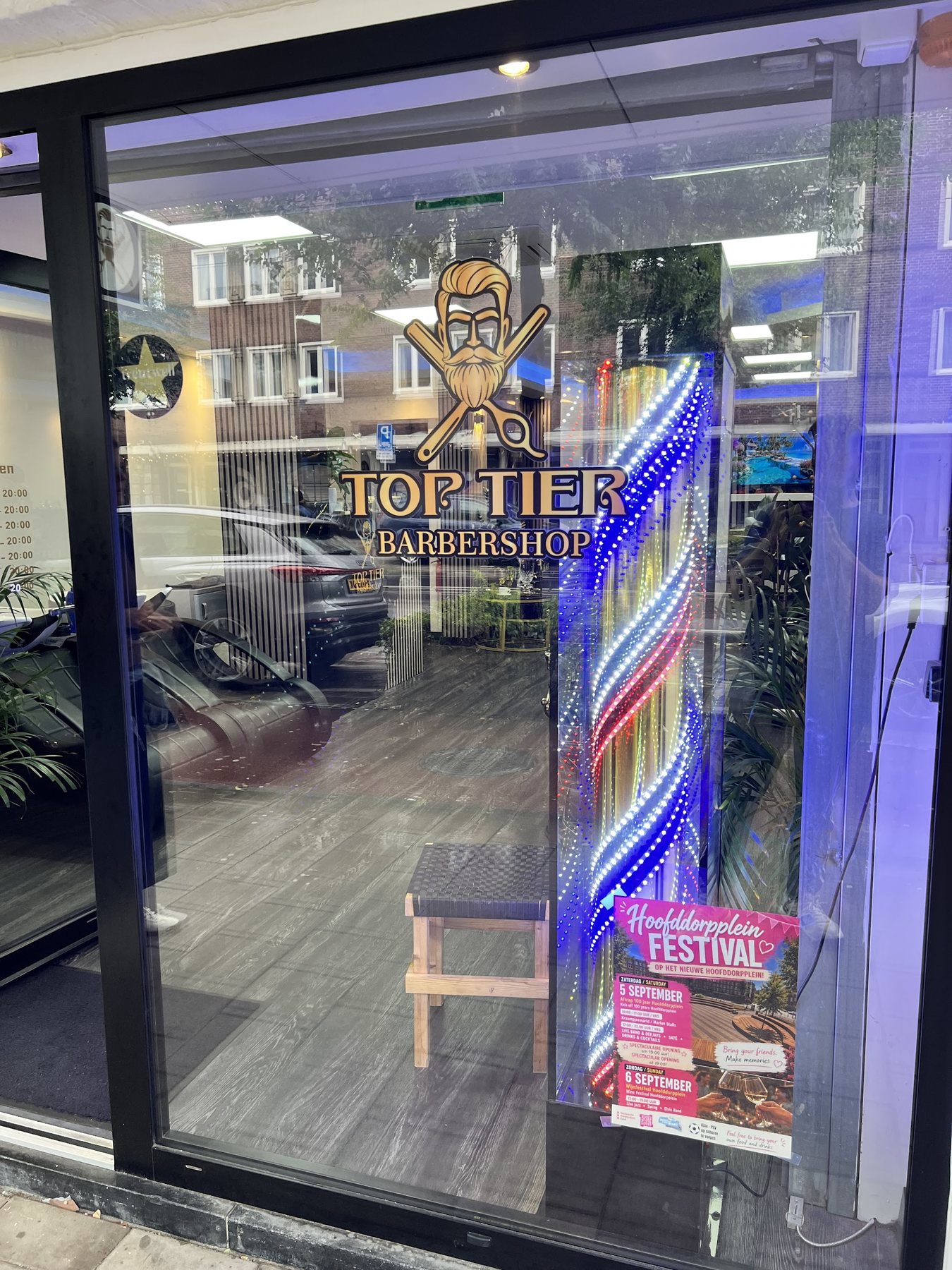 Het raam van de zaak met het gouden Top Tier Barbershop logo en een verlichte barbierspaal