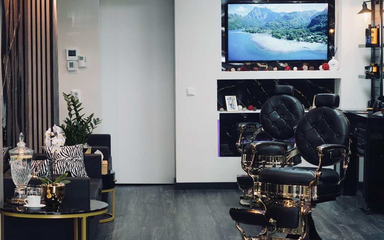 De wachthoek met een glazen karaf op een zwart marmeren tafeltje, naast twee barbierstoelen en een tv aan de wand