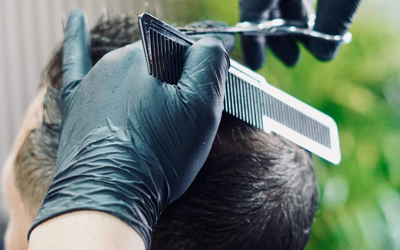 Een hand in zwarte handschoen met kam en schaar, bezig met een knipbeurt